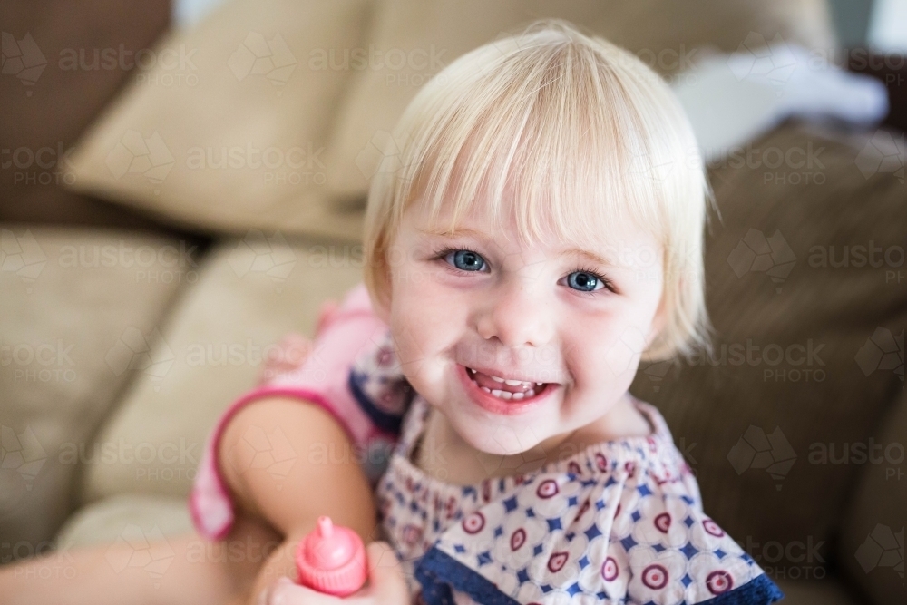 Young blonde girl smiling holding toys at home - Australian Stock Image