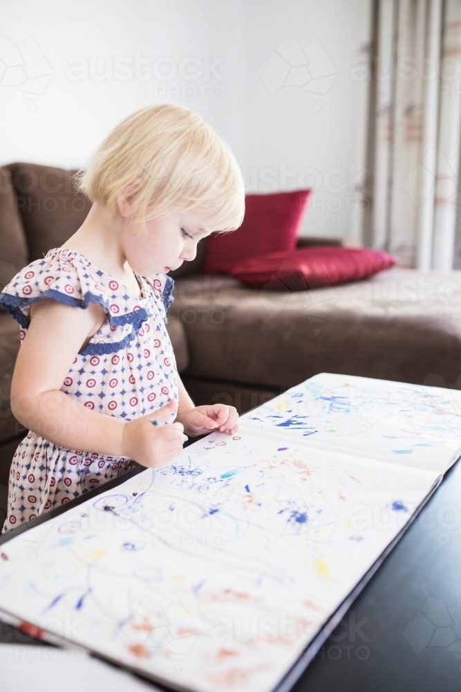 Young blonde girl standing at table colouring in with crayons - Australian Stock Image