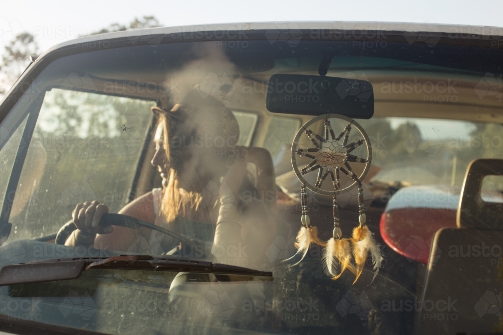 Young bohemian woman driving car into the sunlight - Australian Stock Image