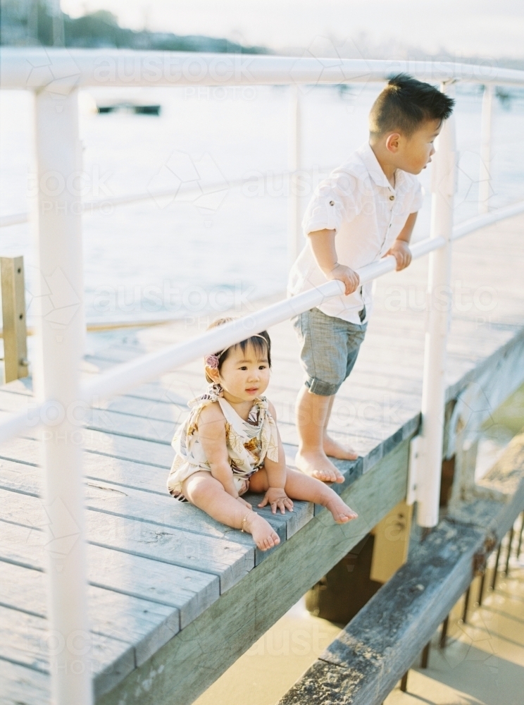 Young boy and baby sister on a wharf at the beach - Australian Stock Image