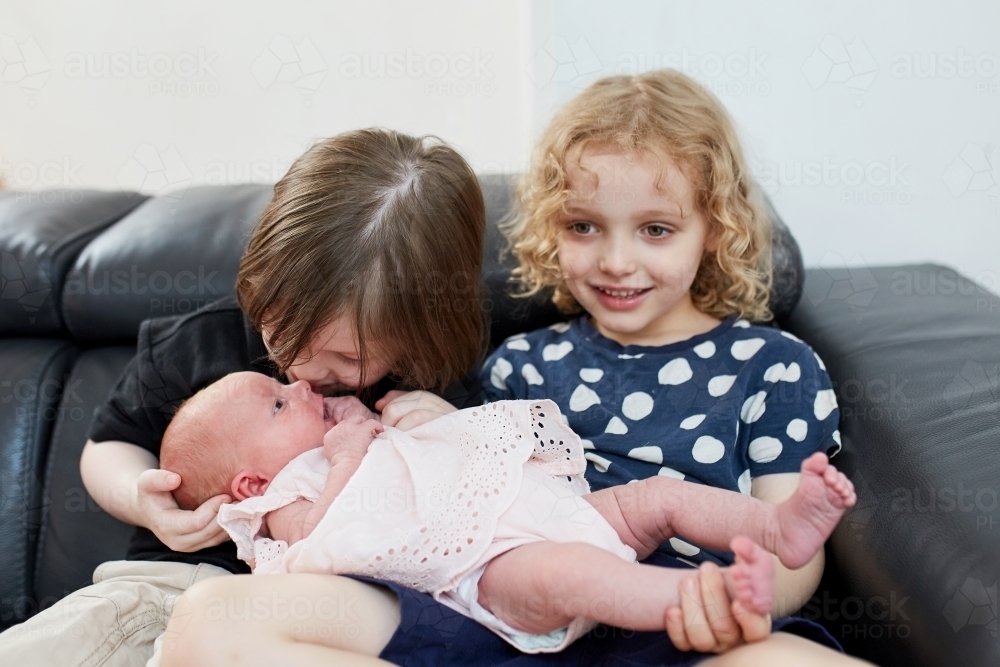 Young boy and girl holding baby, boy kissing baby - Australian Stock Image