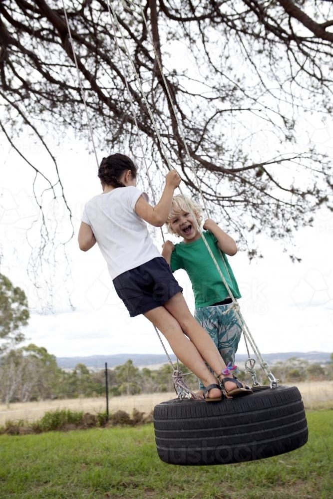 Young boy and girl on a tyre swing in a country backyard - Australian Stock Image