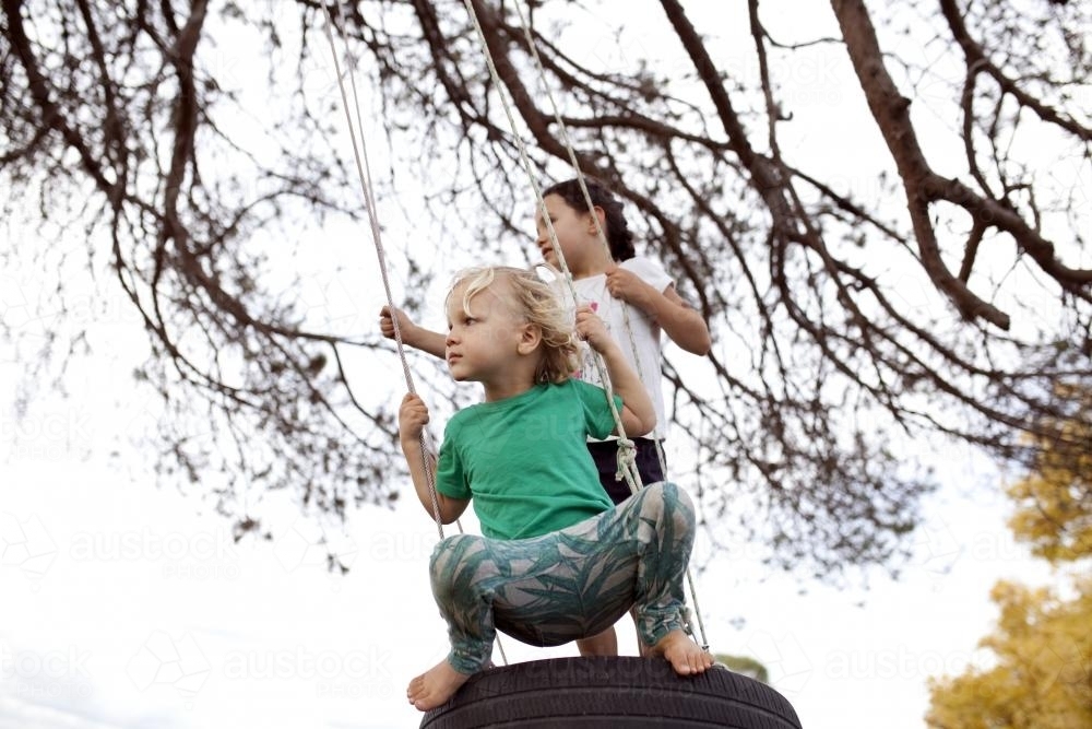 Young boy and girl swinging on tyre swing - Australian Stock Image