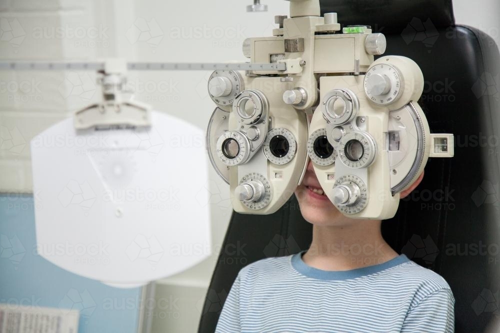 Young boy at an optometrist appointment looking through phoropter - Australian Stock Image