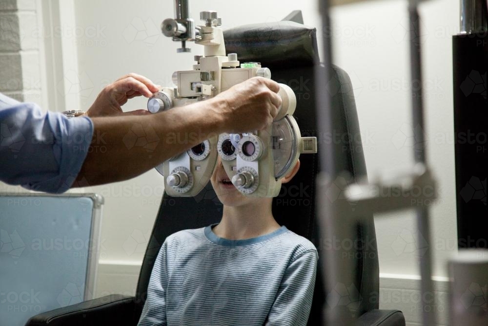 Young boy at an optometrist appointment looking through phoropter - Australian Stock Image