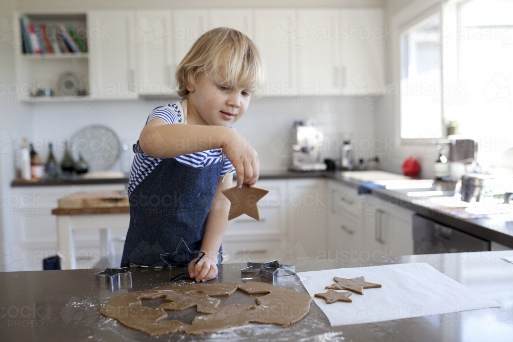 Young boy baking gingerbread cookies in kitchen at home - Australian Stock Image