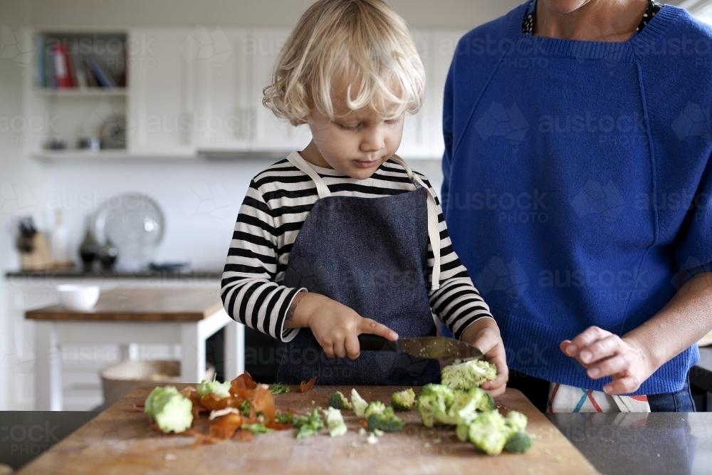 Young boy being supervised while chopping veggies - Australian Stock Image