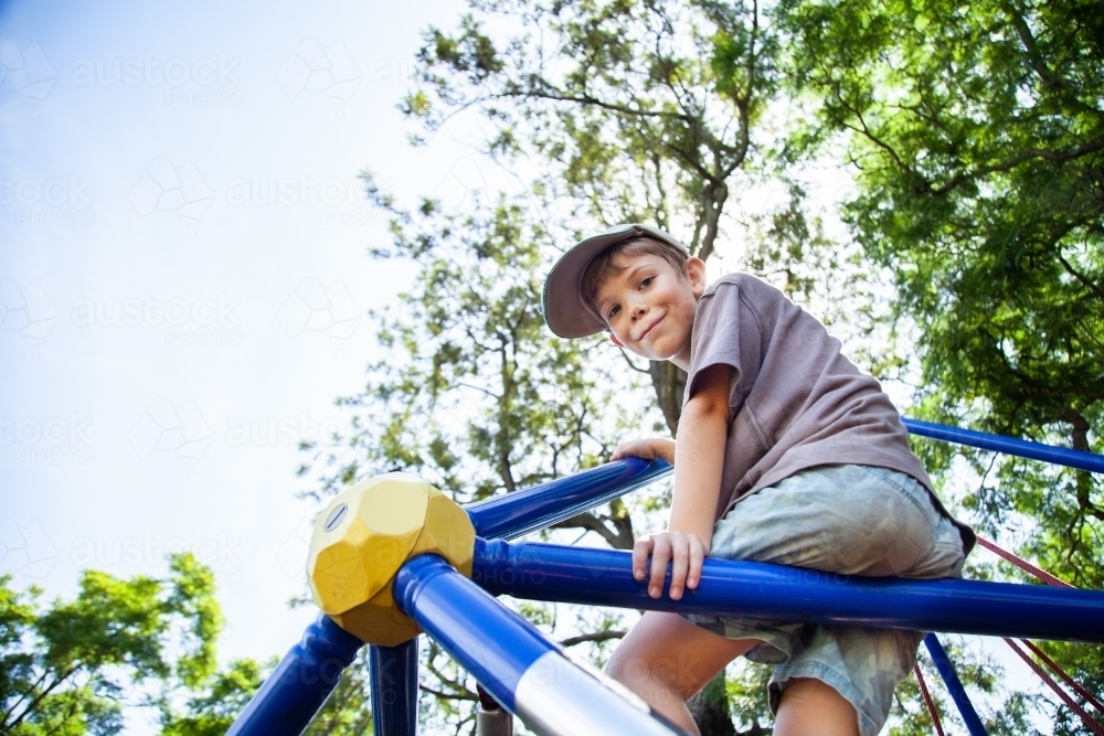 Young boy climbing spiderweb playground equipment at park - Australian Stock Image