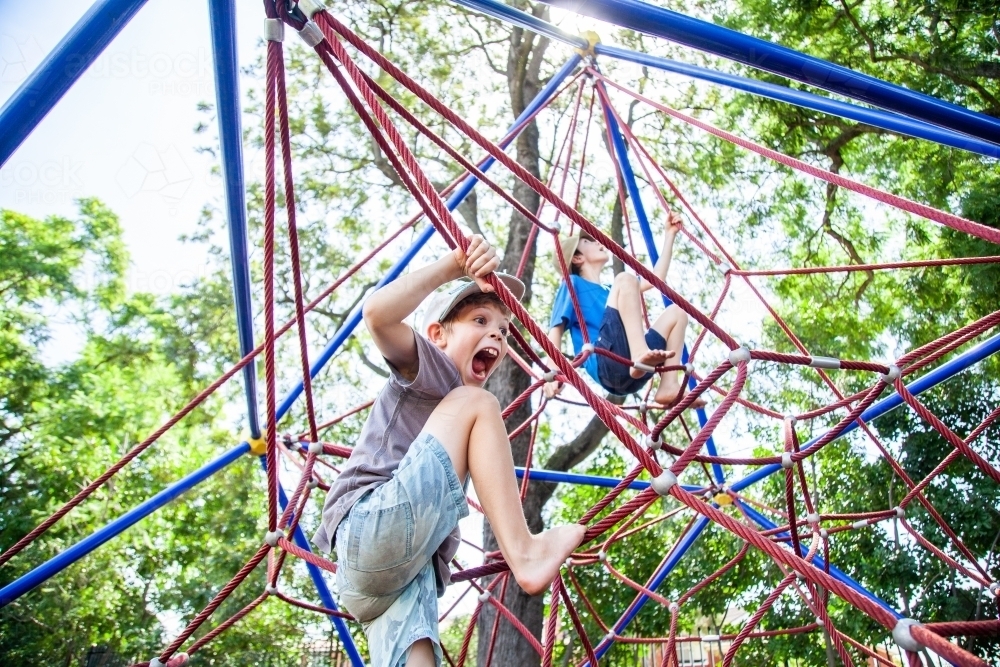 Young boy climbing spiderweb playground equipment at park - Australian Stock Image