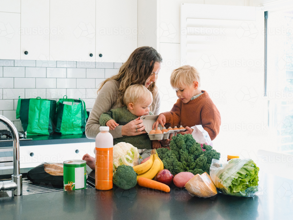 Young boy counting eggs with mum holding the baby on the countertop - Australian Stock Image