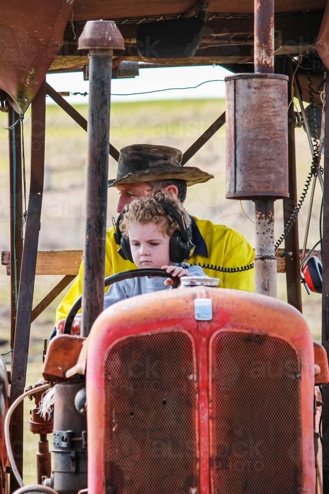 Young boy driving tractor with farmer - Australian Stock Image