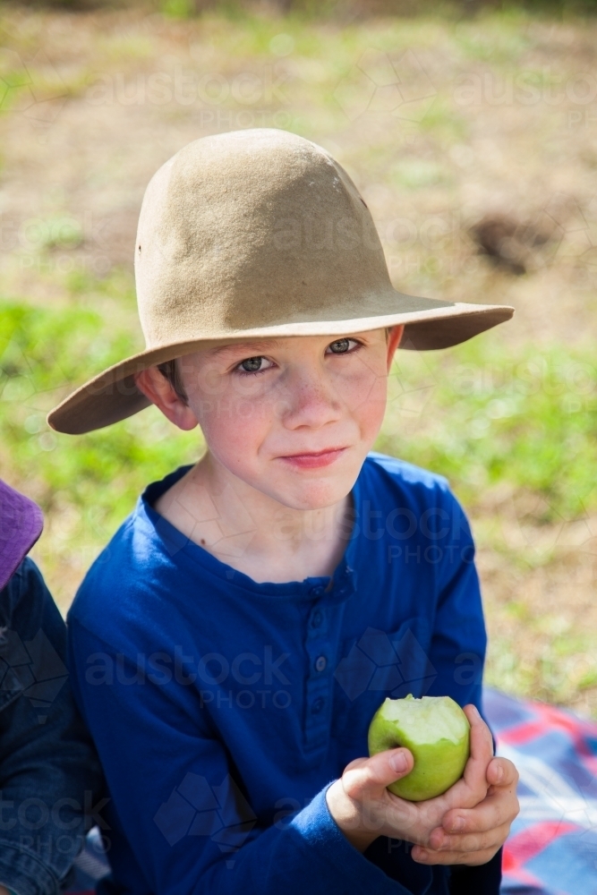 Young boy eating a green apple outside - Australian Stock Image