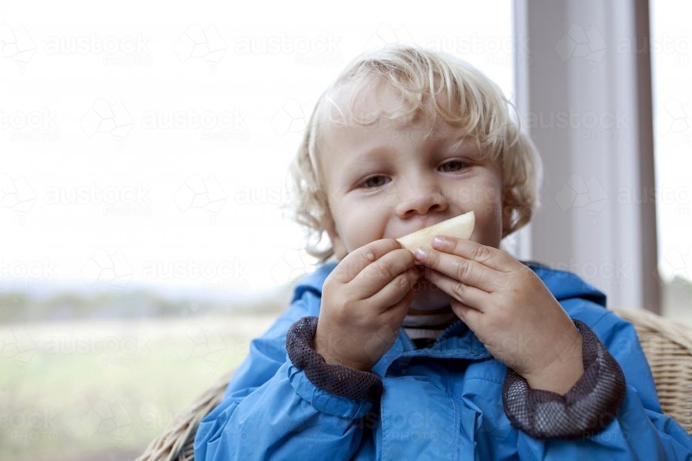 Young boy eating apple and making a funny face - Australian Stock Image