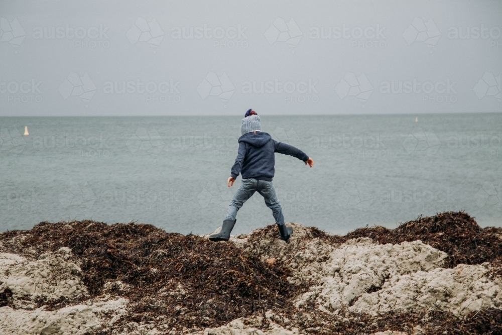 Young boy exploring coastal beach on cold winter day - Australian Stock Image