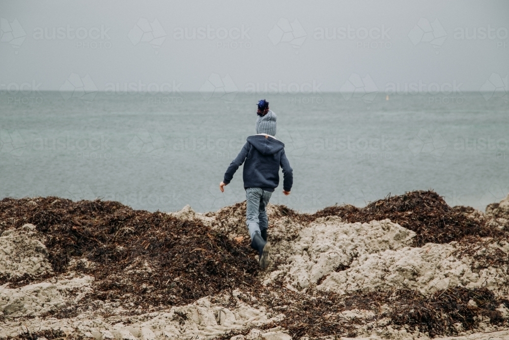 Young boy exploring coastal beach on cold winter day - Australian Stock Image
