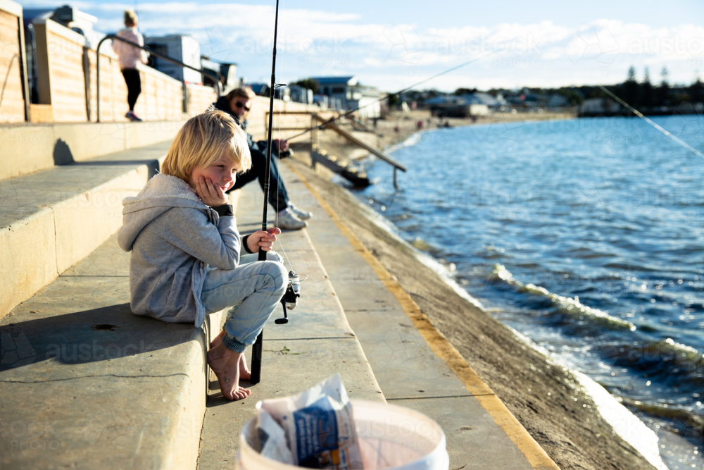 Young boy fishing from concrete steps by the ocean - Australian Stock Image