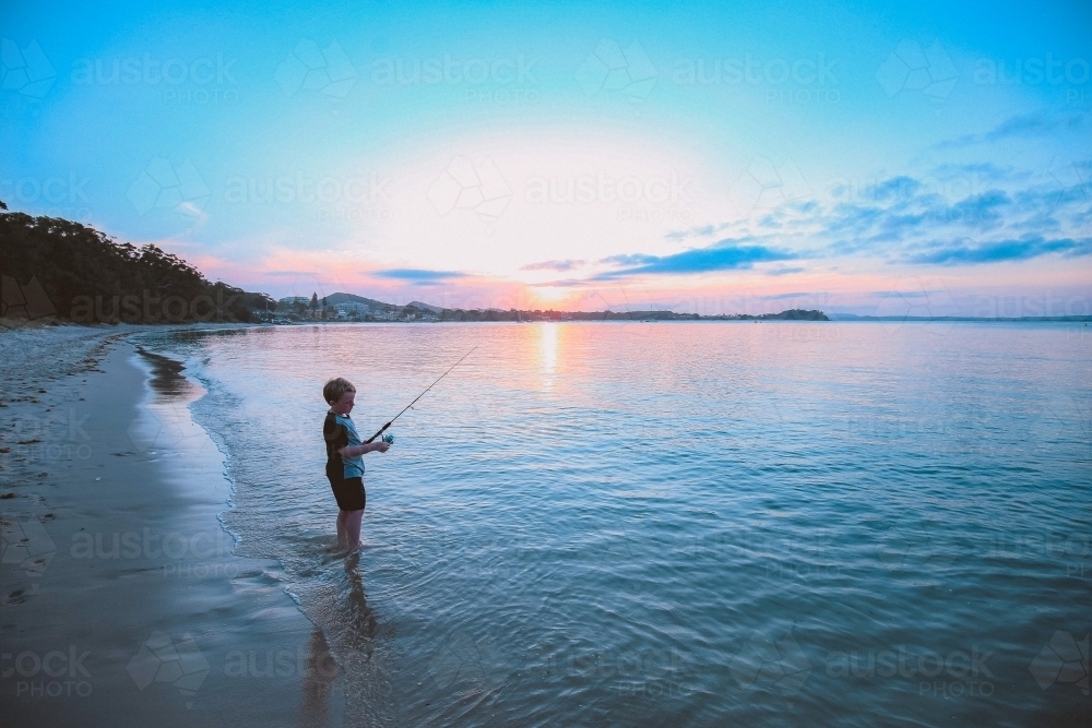 Young boy fishing on the beach at sunset - Australian Stock Image