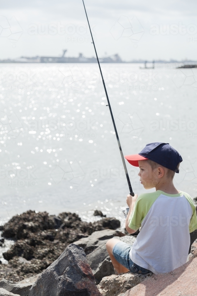 Young boy fishing with rod off rocks at Stockton, Newcastle - Australian Stock Image