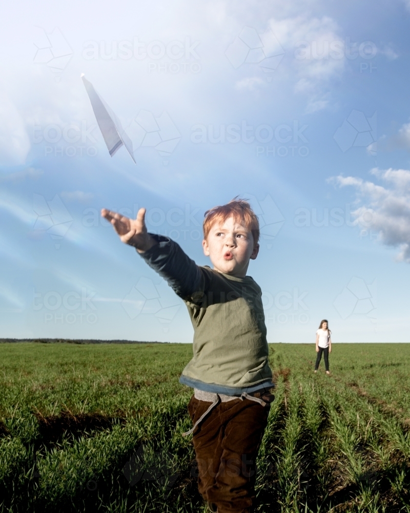 Young boy flying a paper aeroplane in a green farm paddock - Australian Stock Image