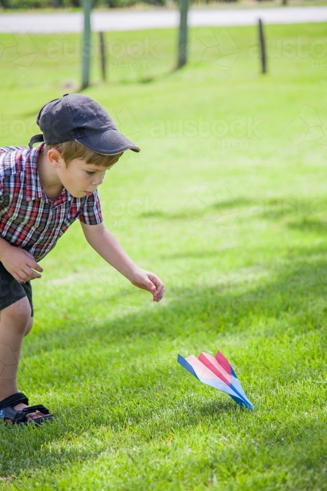 Young boy flying paper plane outside on grass - Australian Stock Image
