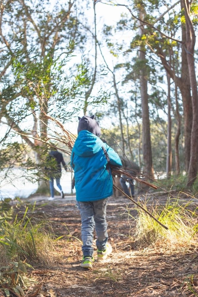 Young boy from behind carrying firewood - Australian Stock Image