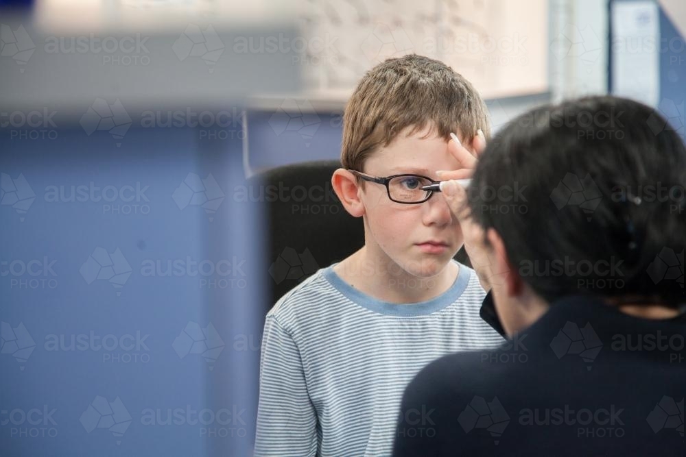 Young boy getting fitted for new glasses at the optometrist - Australian Stock Image