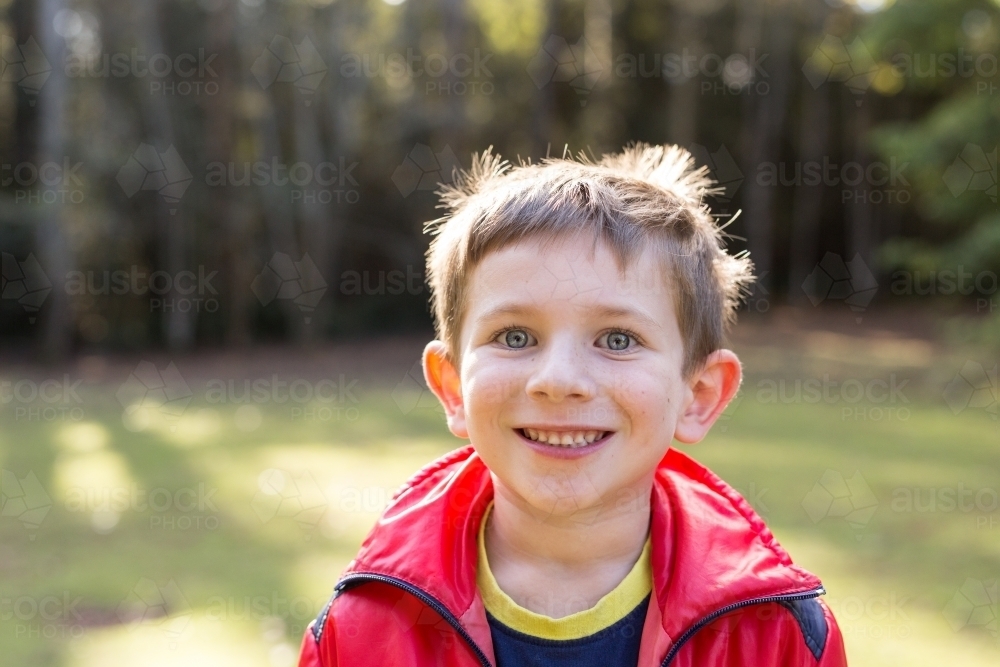 Young boy grinning at camera in forest - Australian Stock Image