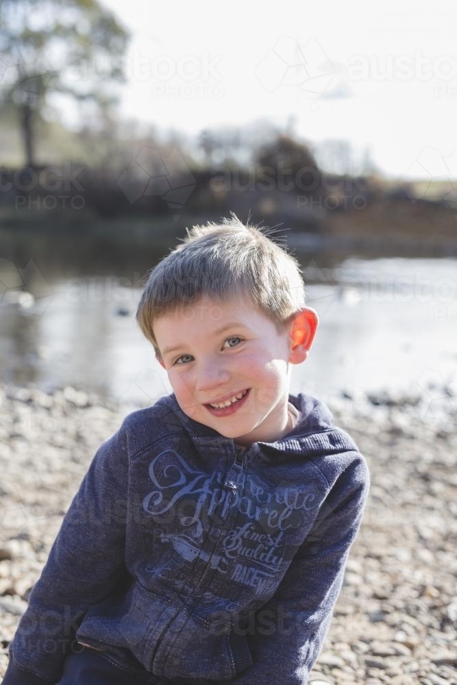 Young boy grinning beside a river - Australian Stock Image
