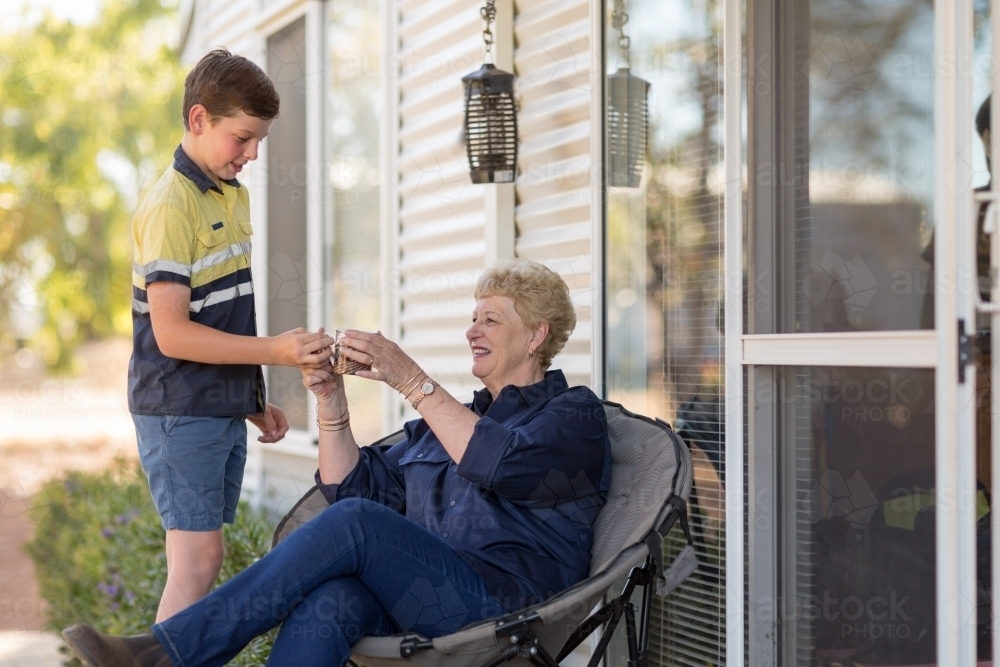 Young boy handing his grandmother a cup of tea - Australian Stock Image