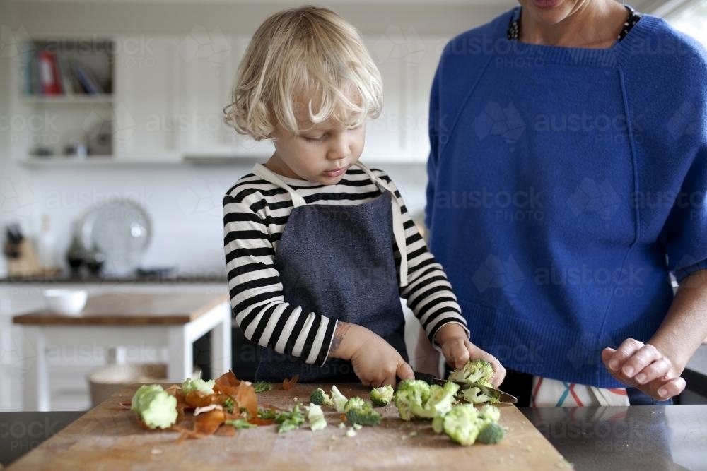 Image of Young boy helping cook by cutting vegetables - Austockphoto