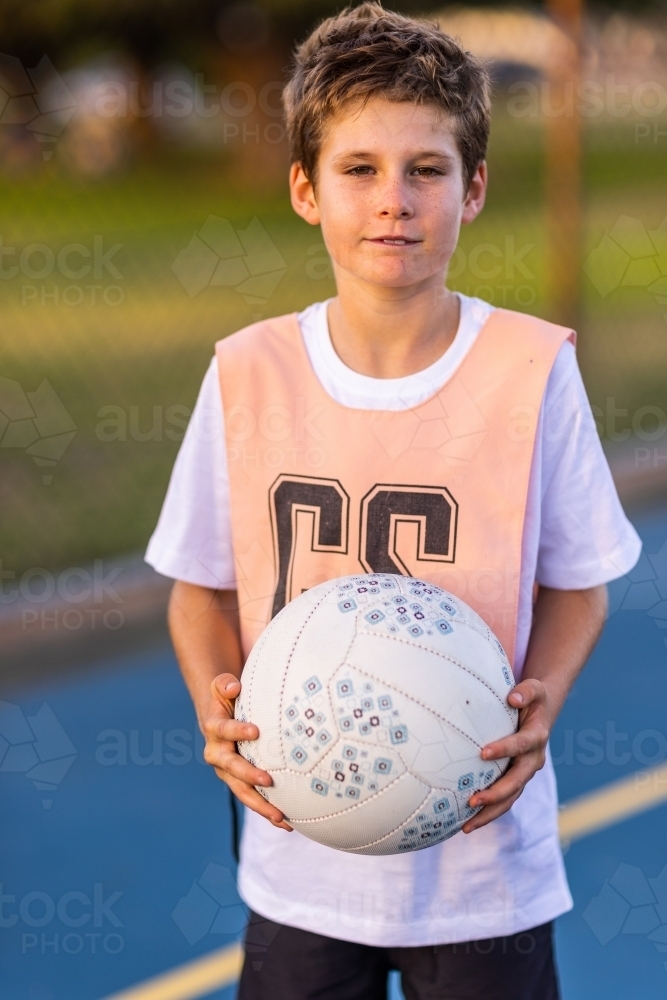 young boy holding a netball and wearing a netball bib - Australian Stock Image