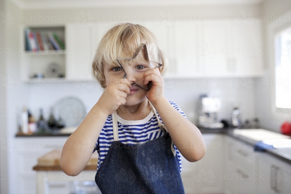 Young boy holding cookie cutter shape up in front of face - Australian Stock Image