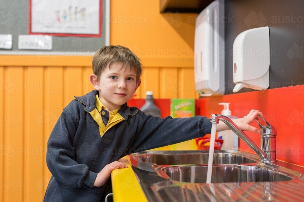Young boy in classroom turning on tap - Australian Stock Image