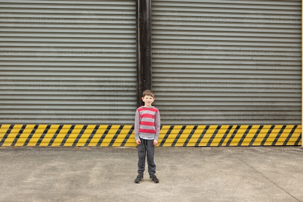 Young boy in front of large roller door - Australian Stock Image