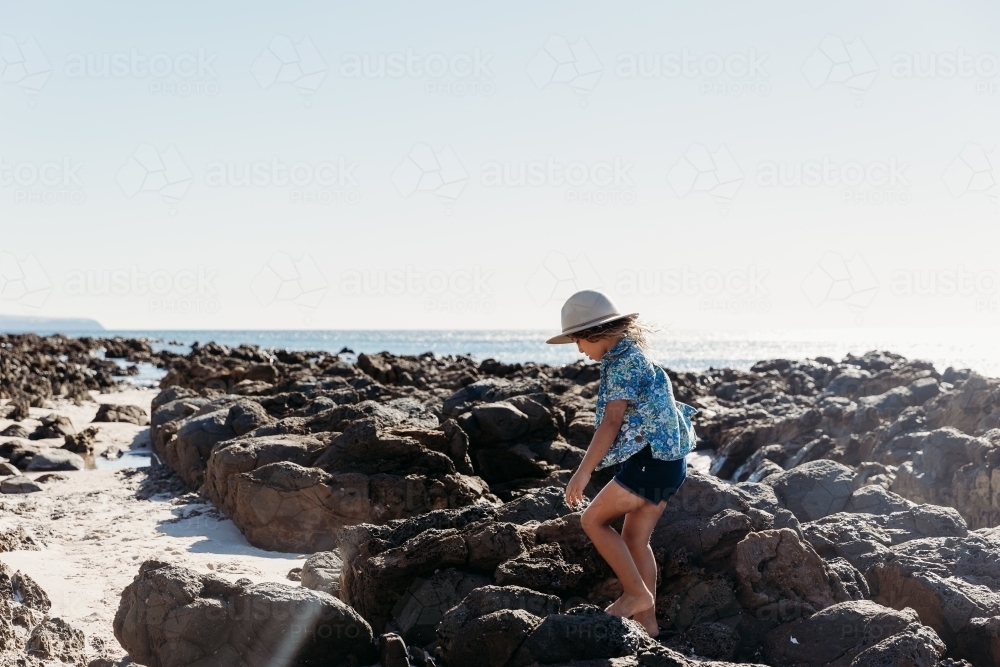 Young boy in hat walking amongst rock pools - Australian Stock Image