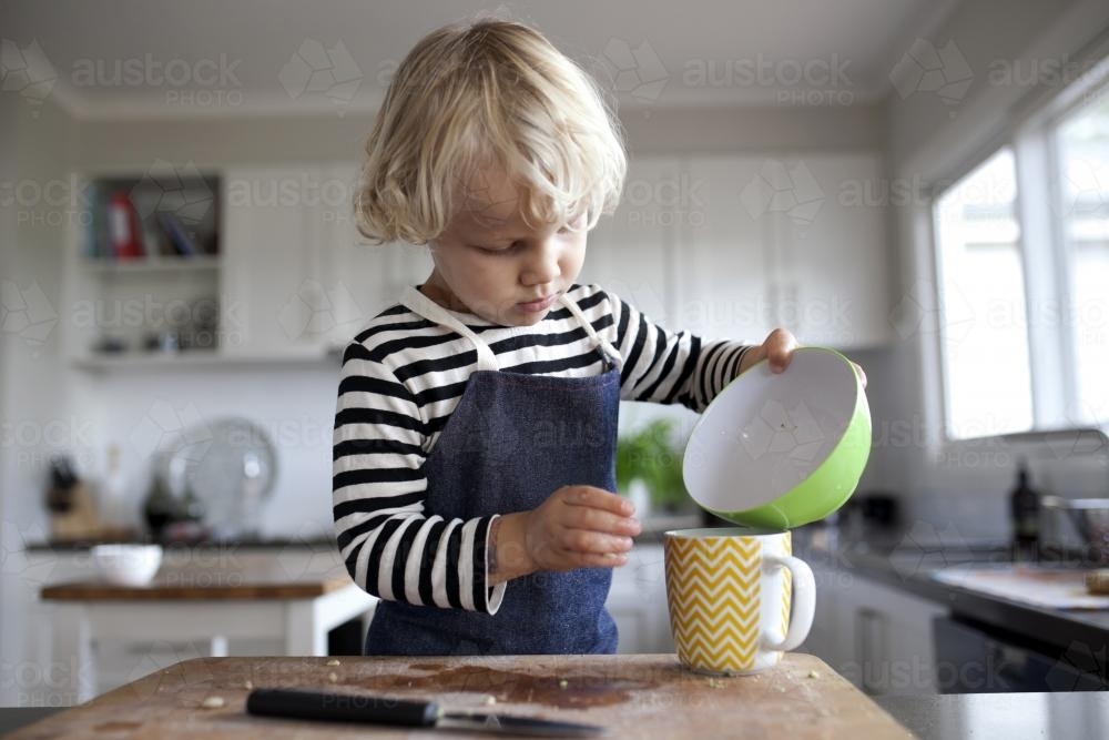 Young boy in kitchen pouring liquid from bowl to cup - Australian Stock Image