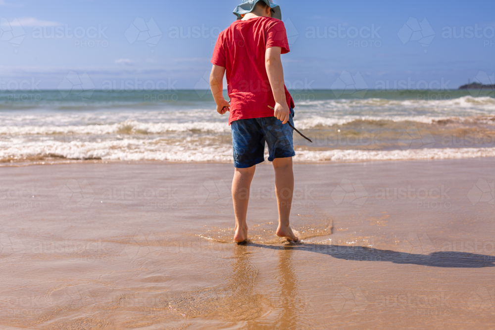 young boy in red shirt and blue shorts on the beach - Australian Stock Image