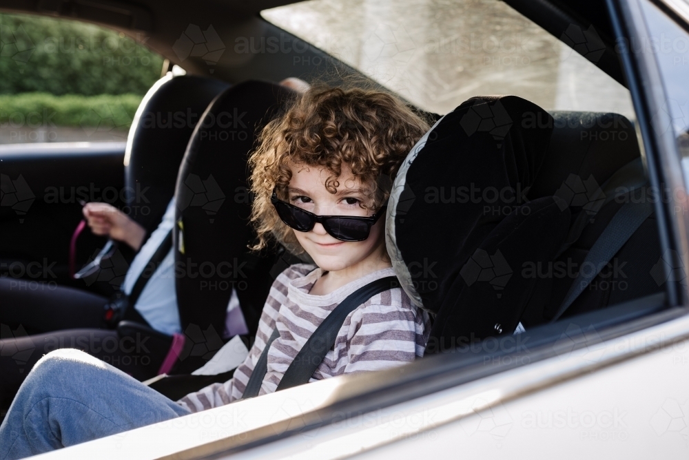Young boy in the backseat of the family car with his sunglasses sitting down over his nose - Australian Stock Image