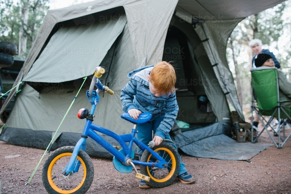 Young boy inspecting his bike at a camp site - Australian Stock Image