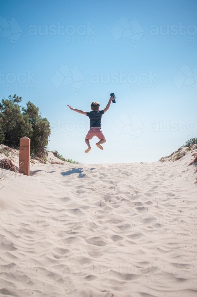 Young boy jumping in the air on white sandy beach - Australian Stock Image