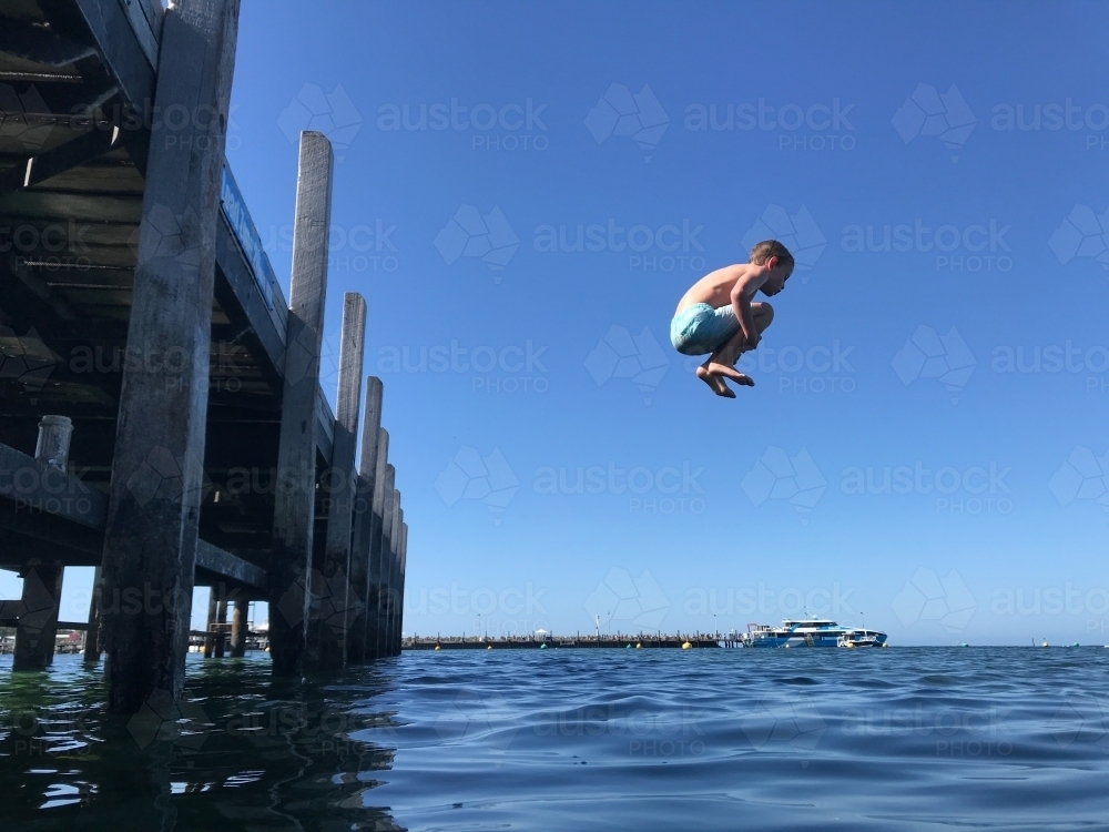 Image of Young boy jumping off jetty caught mid air over the ocean ...