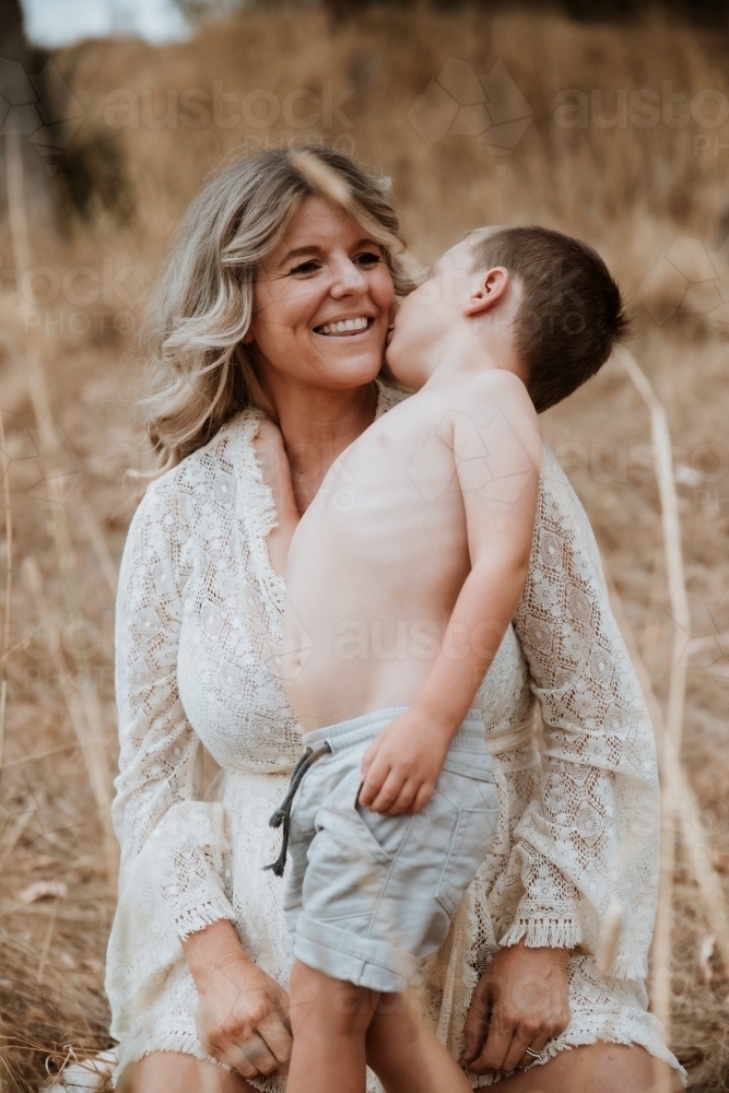 Young boy kissing his mother's cheek in a field of long grass - Australian Stock Image