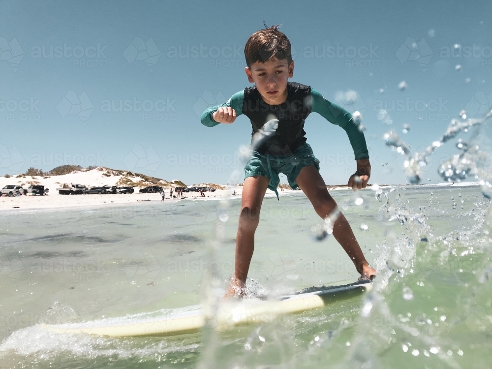 Young boy learning to surf on longboard with sprays of water on lens - Australian Stock Image
