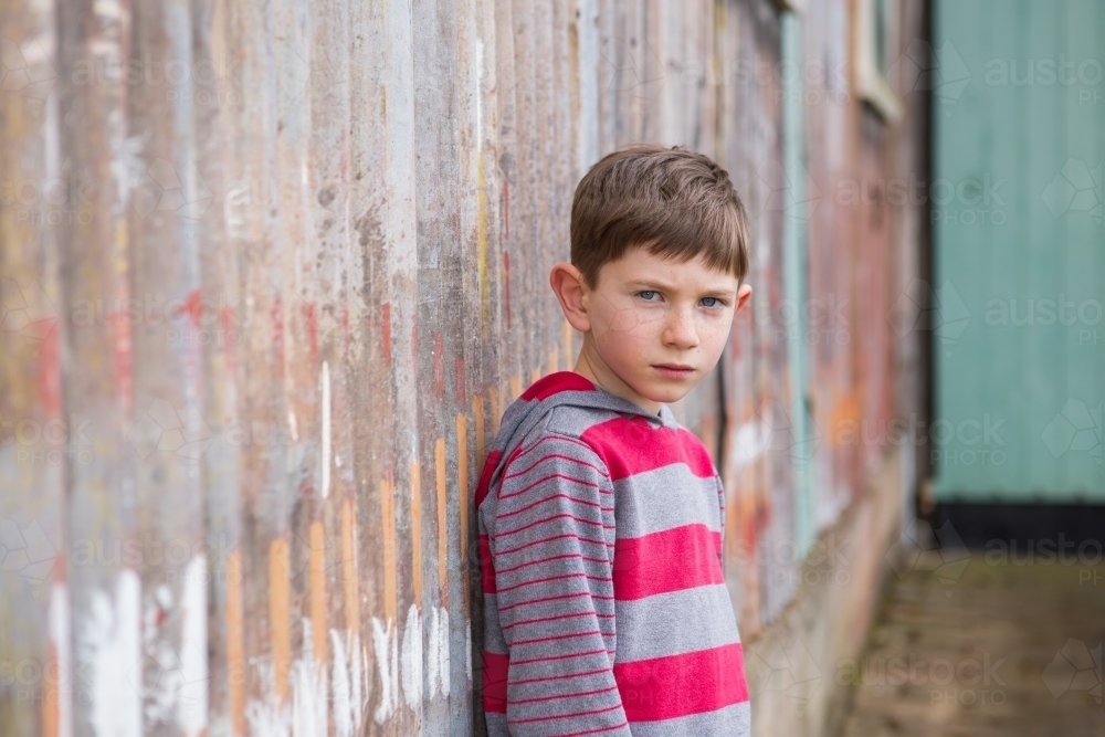 Young boy looking at camera in front of rusty iron wall - Australian Stock Image