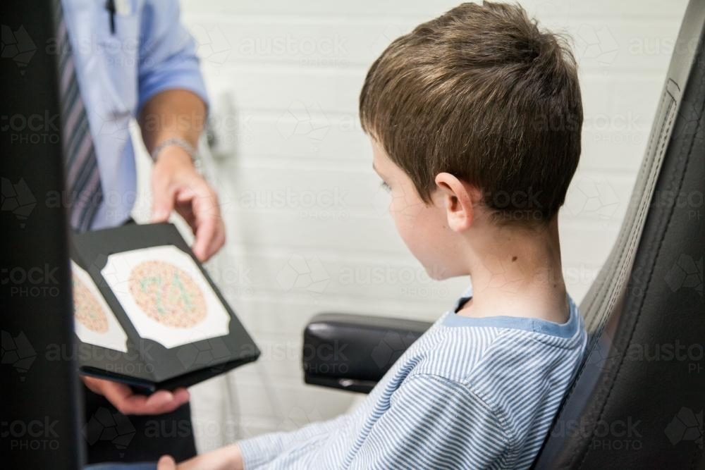 Young boy looking at optometrists book  for colour blind eye test - Australian Stock Image