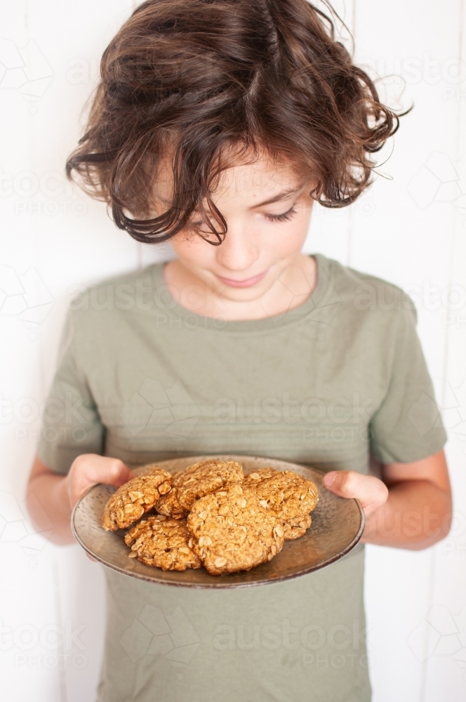 Young boy looking down at plate of biscuits he is holding - Australian Stock Image