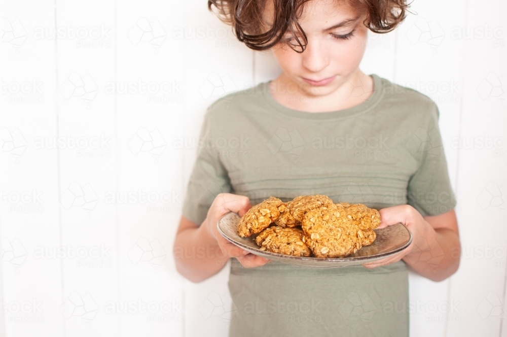 Young boy looking down at plate of cookies he is holding - Australian Stock Image
