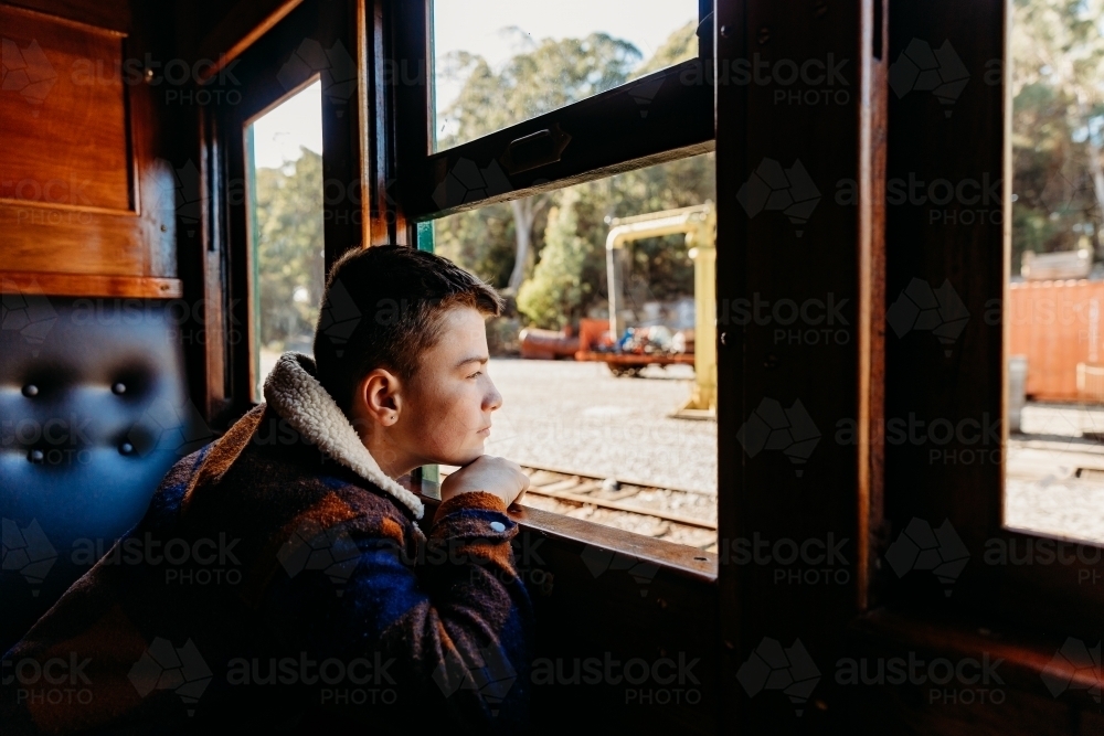 Young boy looking out open window on train - Australian Stock Image