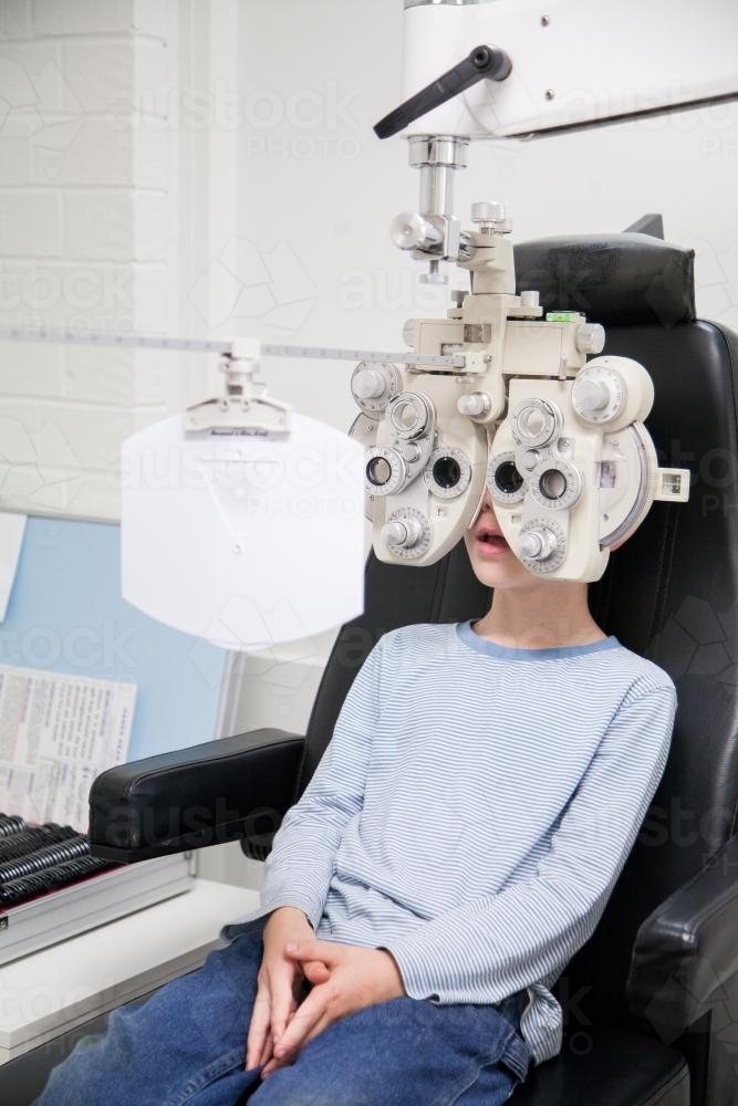 Young boy looking through phoropter during eye examination - Australian Stock Image