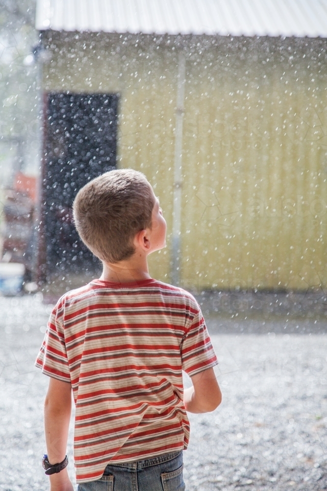 Young boy looking up at falling rain - Australian Stock Image